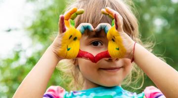 Image shows a young girl holding her painted hands in a heart shape
