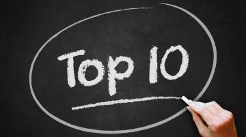 Image shows a hand writing on a blackboard the words top ten