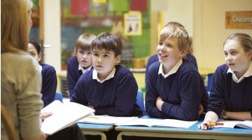 Image shows a teacher sitting in front of a class of primary school pupils 