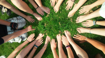 a group of people sitting on grass with their hands in a circle