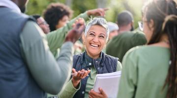 Image shows a lady smiling holding a notepad talking to a group of people 