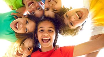 Group portrait of happy kids huddling, looking down at camera and smiling.