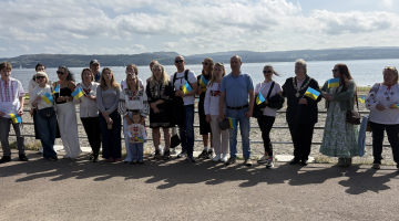 A group of people stand in front of the railings at the sea front in Dunoon