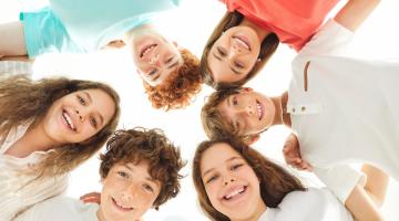 Image shows a group of six teenagers in a circle smiling looking down the camera 