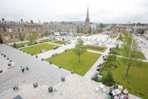 An aerial image of Helensburgh's Colquhoun Square. To the bottom right of the image, a group of people are sitting at a cafe table. 
