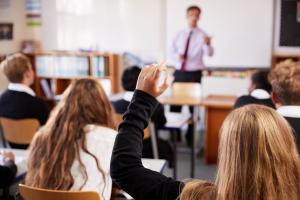 Image shows a classroom with a teacher standing at the front with pupils looking at him