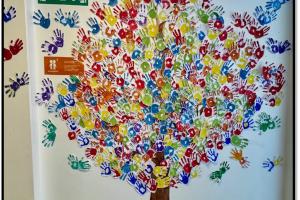 image shows a picture of a tree with hand prints of school children forming the branches 