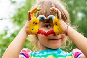 Image shows a young girl holding her painted hands in a heart shape