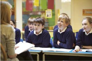 Image shows a teacher sitting in front of a class of primary school pupils 