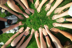 a group of people sitting on grass with their hands in a circle